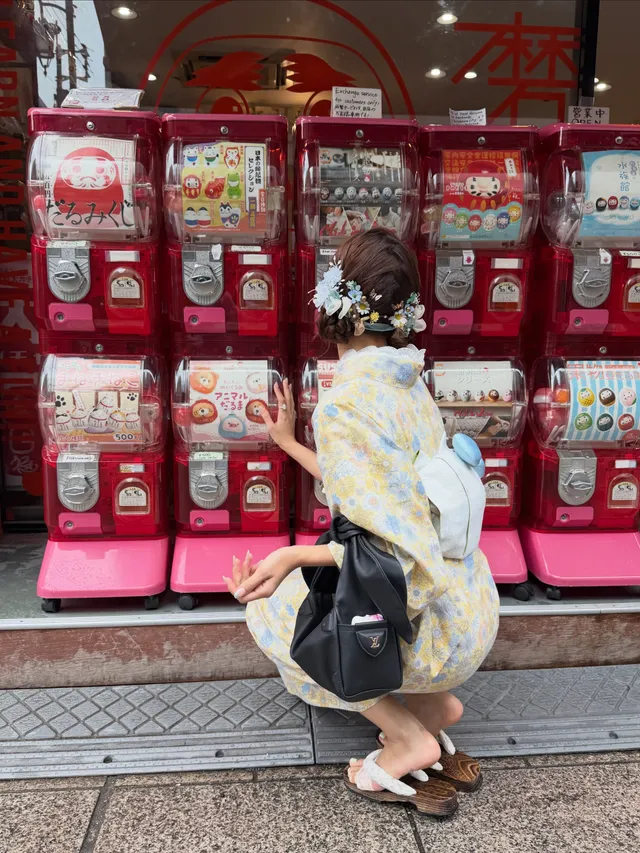 Lisa (Lalisa Manobal) crouching in white flat sandals beside toy-vending machines.