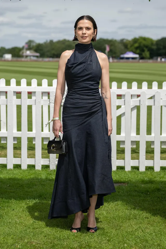 Hayley Atwell standing beside a fence with a small handbag.