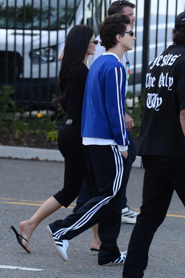 Kylie Jenner walking with a group outdoors wearing black flip flops.