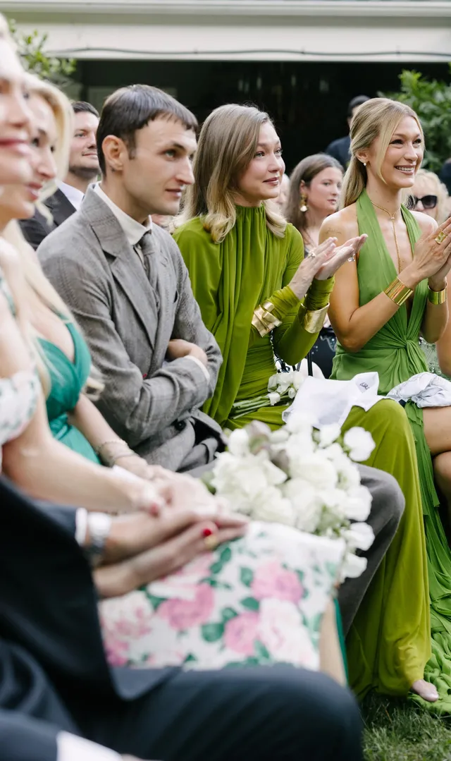 Gigi Hadid sitting with guests in a green dress outdoors.