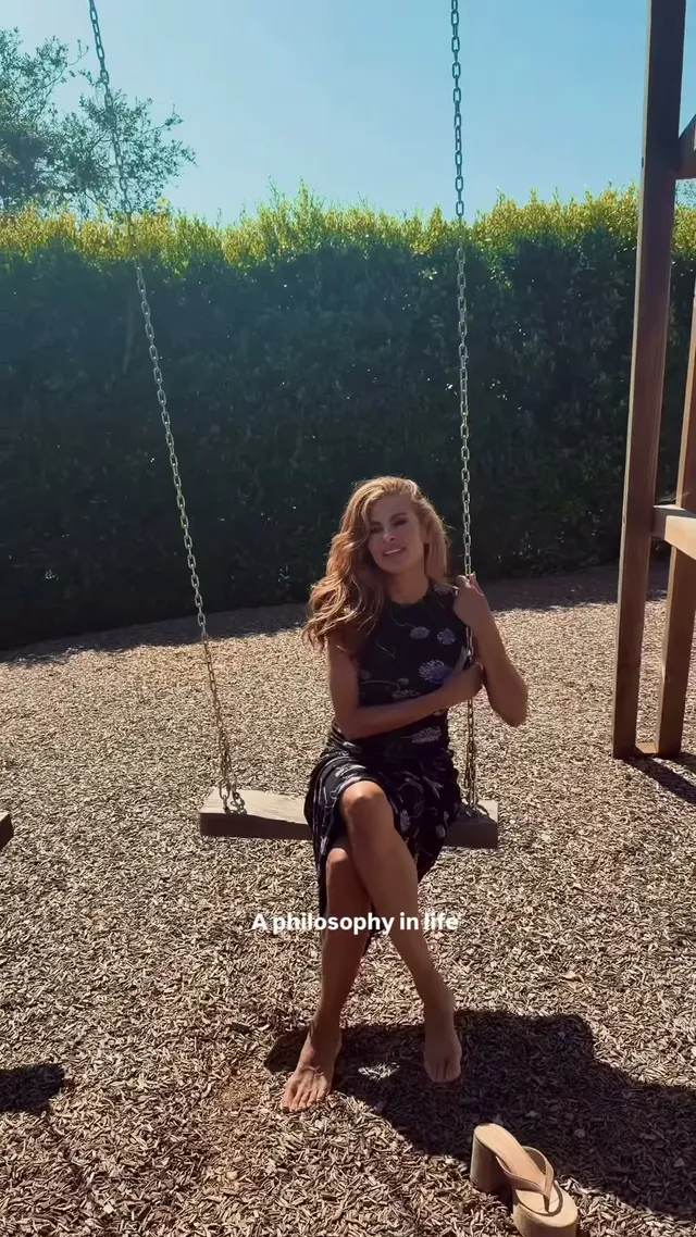 Eva Mendes sitting on a wooden garden swing.