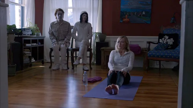 Kirsten Dunst sitting on an exercise mat while two people stand nearby.