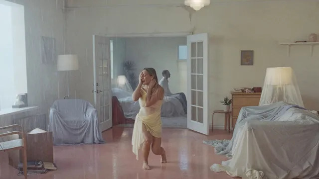 Hilary Duff walking barefoot through a bright bedroom in a pale dress.