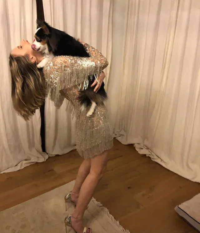 Halston Sage holding a dog while wearing a sparkling mini dress and metallic heels.