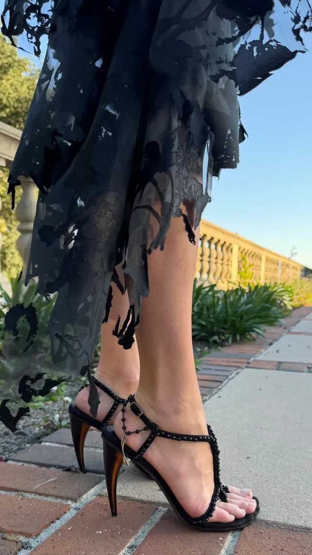 Margot Robbie: close view of black high heels outdoors.