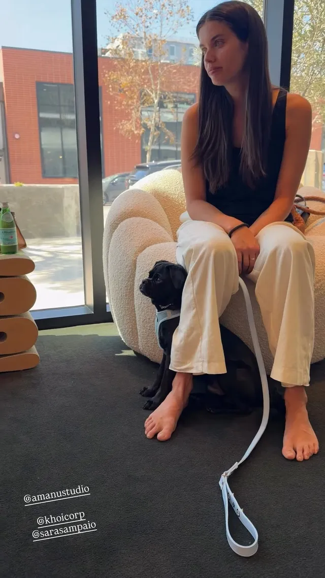 Sara Sampaio sitting barefoot in a white chair beside a window.