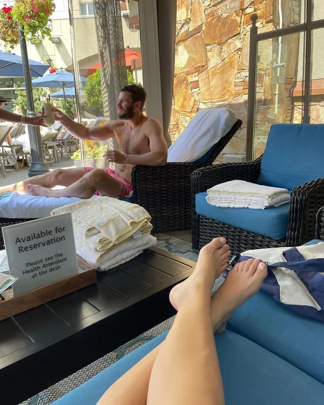 Melissa Barrera relaxing with her bare feet crossed on a blue sun lounger.