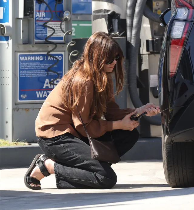 Elizabeth Olsen crouching beside a car wearing black open toe heels.