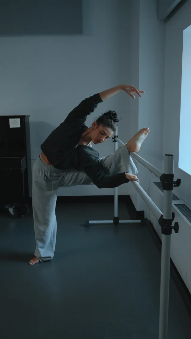 Charli D’Amelio holding a barefoot balance beside a ballet barre.
