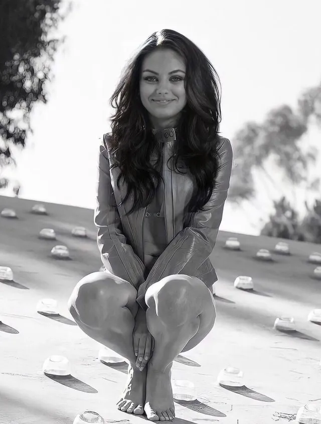 Mila Kunis crouching barefoot in a monochrome portrait.