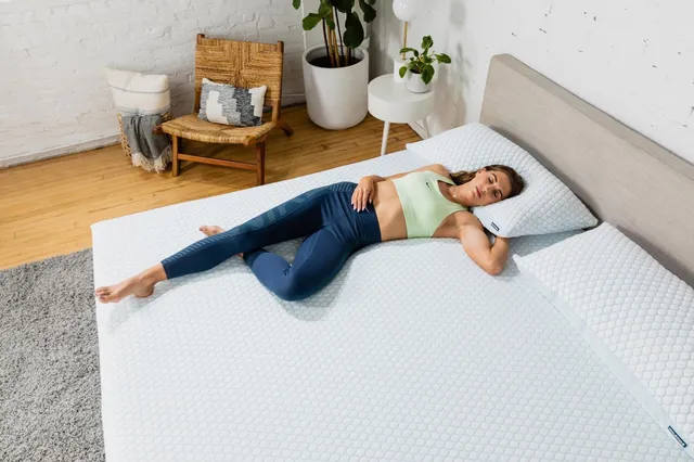Alex Morgan reclining barefoot on a mattress in a green top and blue trousers.