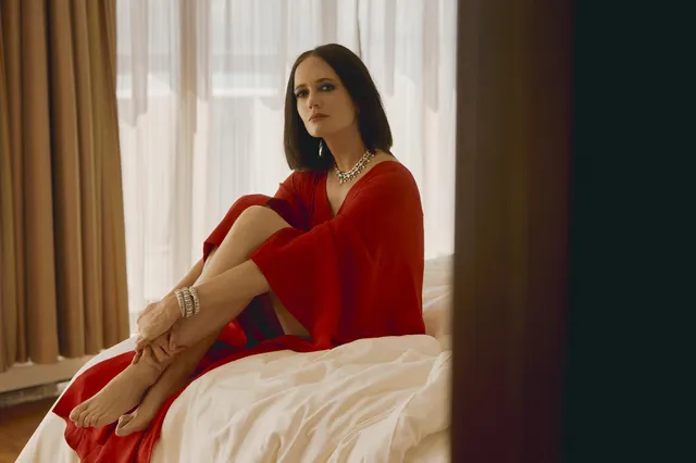 Eva Green seated on a bed in a red dress.