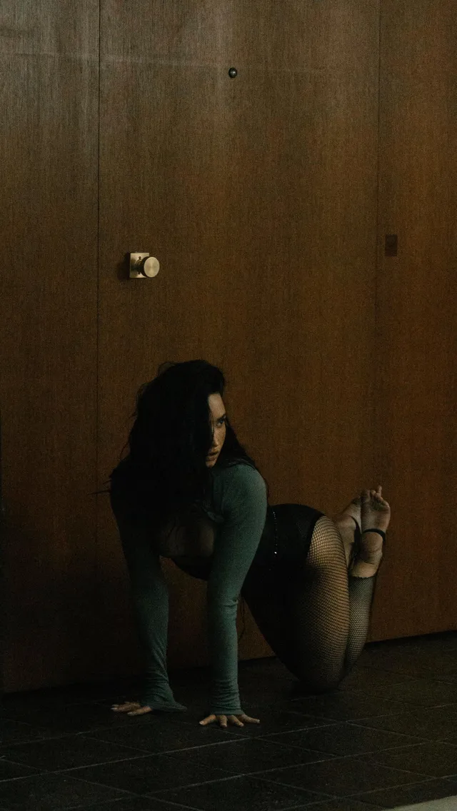 Demi Lovato sitting on a wooden floor with a bare sole raised.