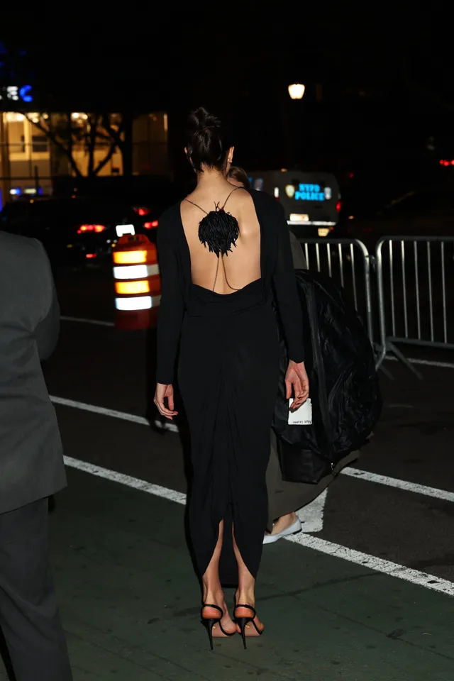 Margaret Qualley walking away in a black dress and heeled sandals.