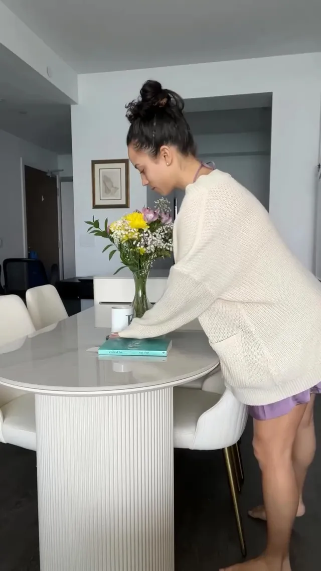 Kiana Madeira standing barefoot at a kitchen table in a pale cardigan.