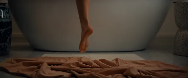 Madelyn Cline raising a bare foot beside a bathtub.