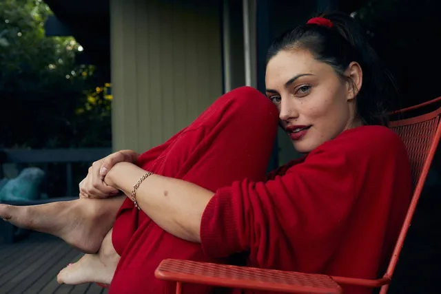 Phoebe Tonkin sitting curled up in a chair wearing a red outfit.