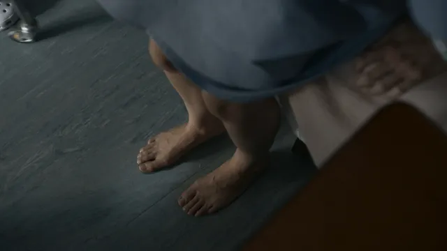 Jodie Comer standing beside a bed in a screen scene.