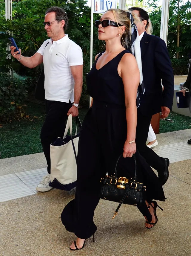 Florence Pugh walking outside in a dark outfit and black heels.