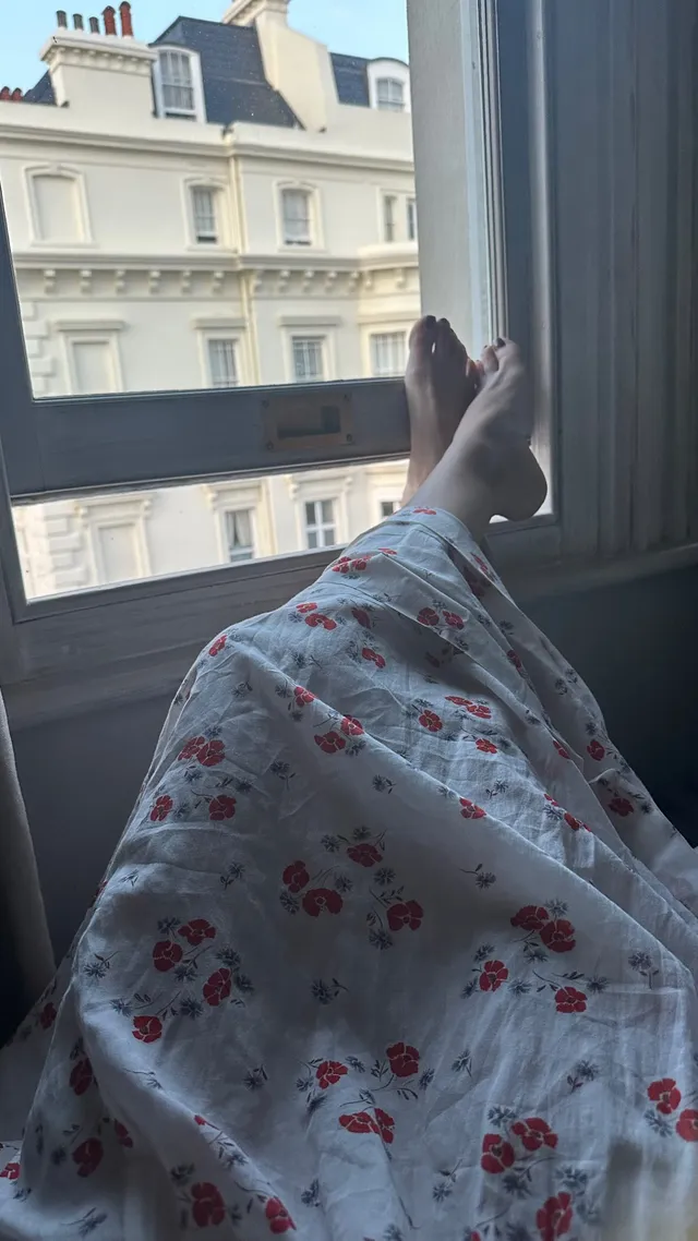 Rachel Bilson resting beside a window in floral trousers.