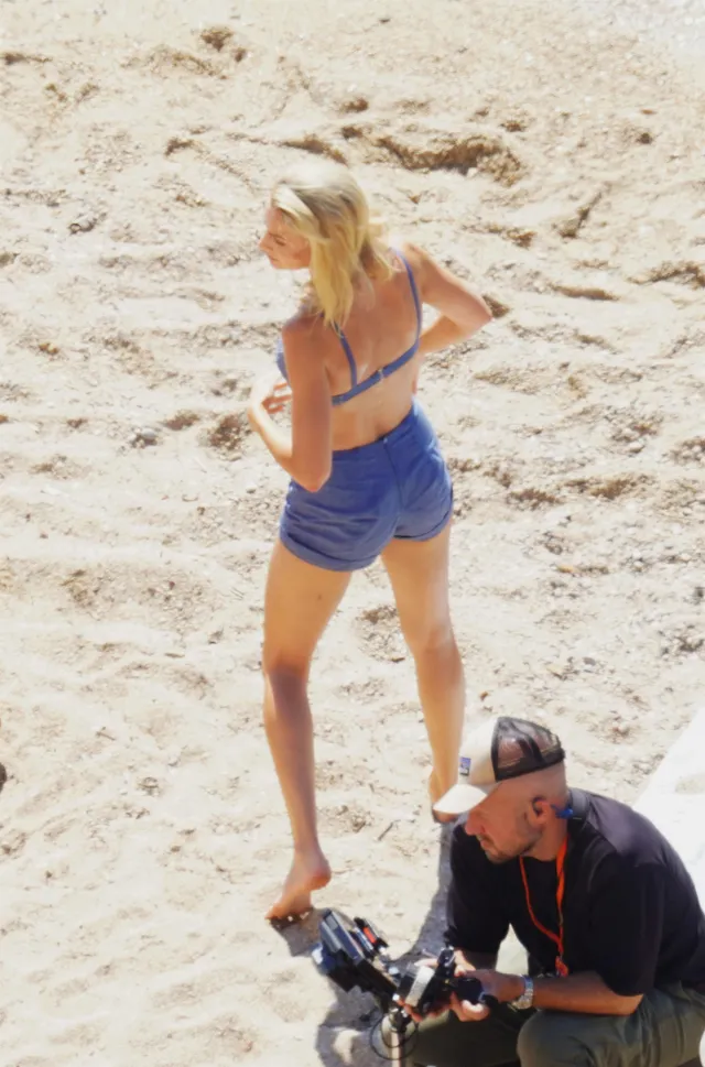 Margot Robbie standing barefoot on a beach wearing a blue outfit.