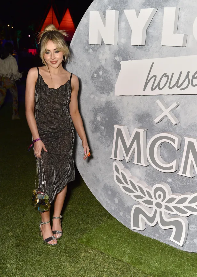Sabrina Carpenter posing in a dark dress and heeled sandals at an event.