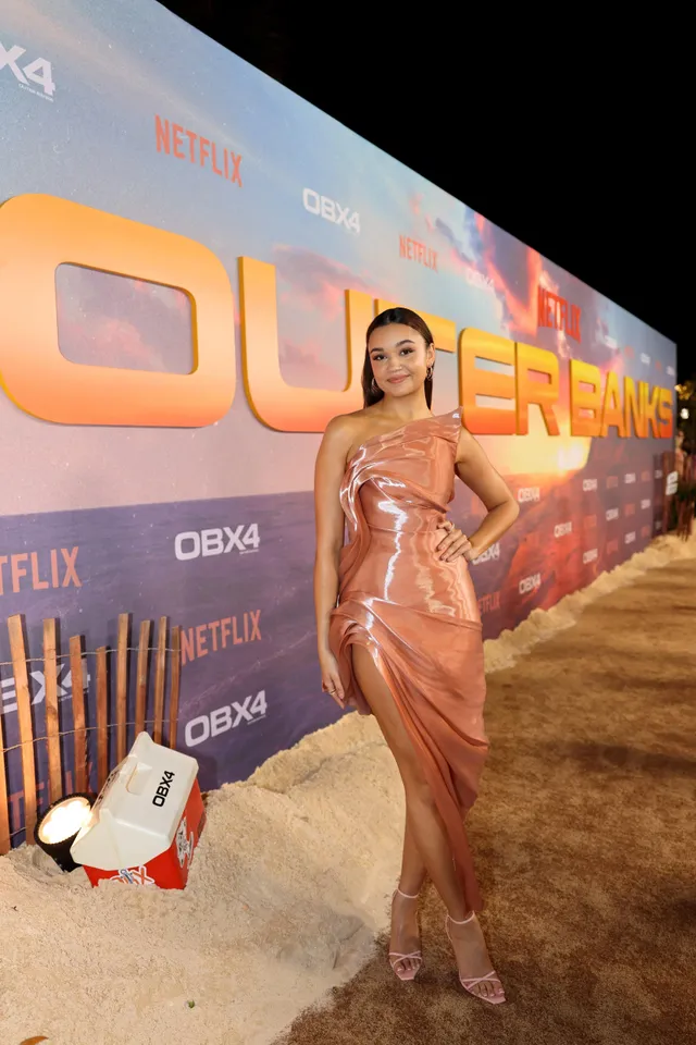 Madison Bailey posing in a bronze dress and pale heels at a premiere.