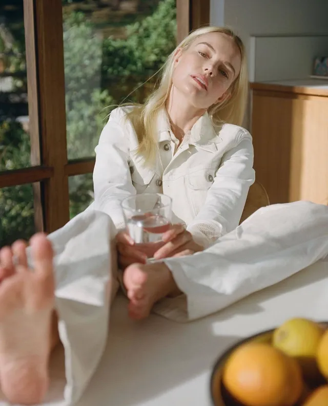 Kate Bosworth sitting in a white outfit with a glass in a fashion portrait.