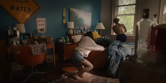 Lola Tung crouching barefoot beside a bed in a scene.