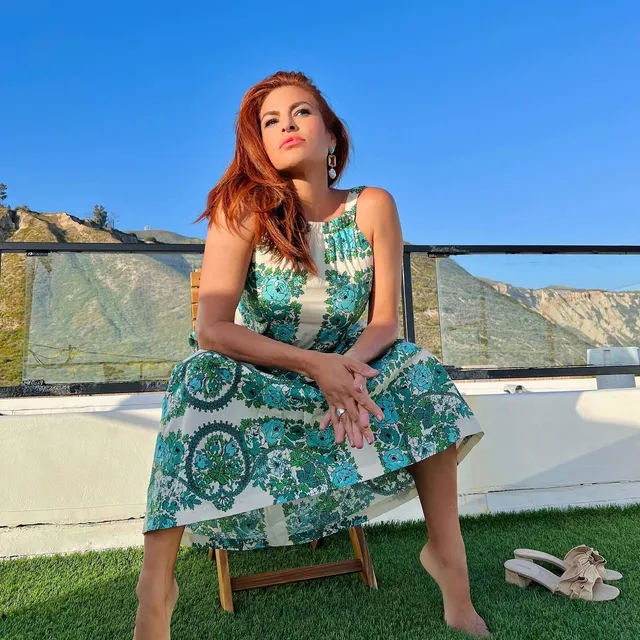 Eva Mendes sitting in a garden chair in a green dress.