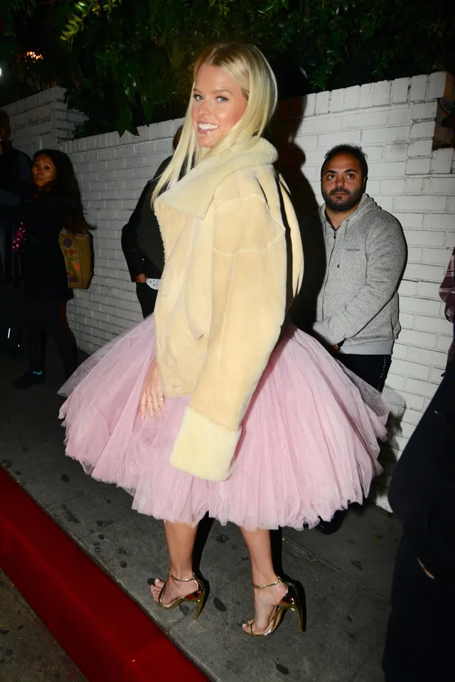 Alice Eve walking outside in a pink skirt and pale coat.
