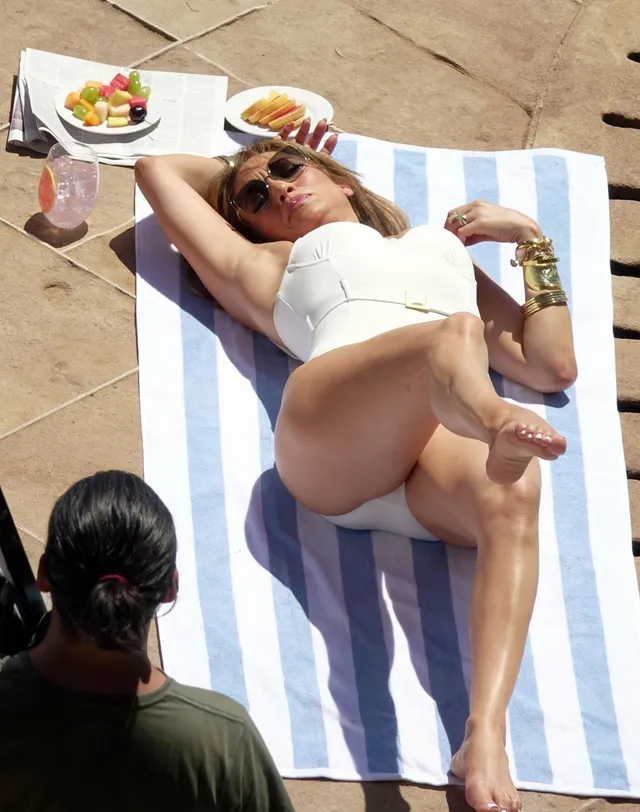 Jennifer Lopez reclining on a striped poolside sunbed.