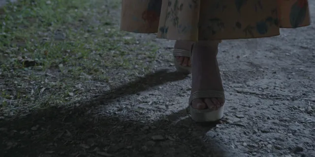 Anna Kendrick walking along a path in pale heeled shoes.