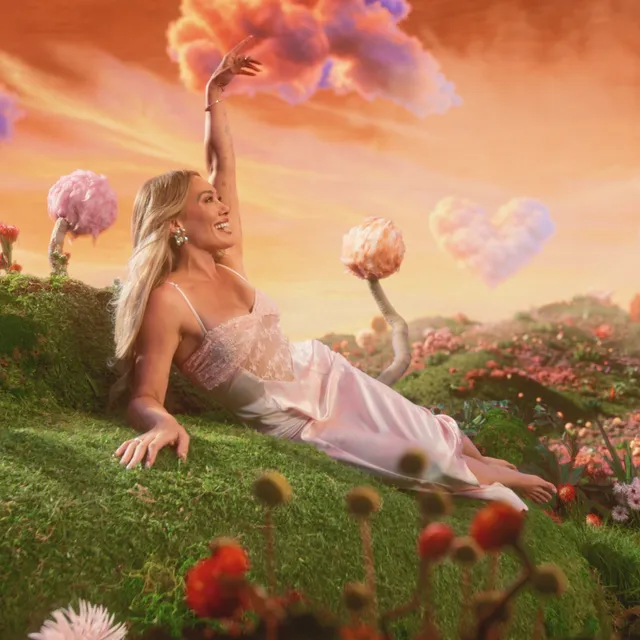 Hilary Duff reclining barefoot amid flowers in a colorful studio scene.