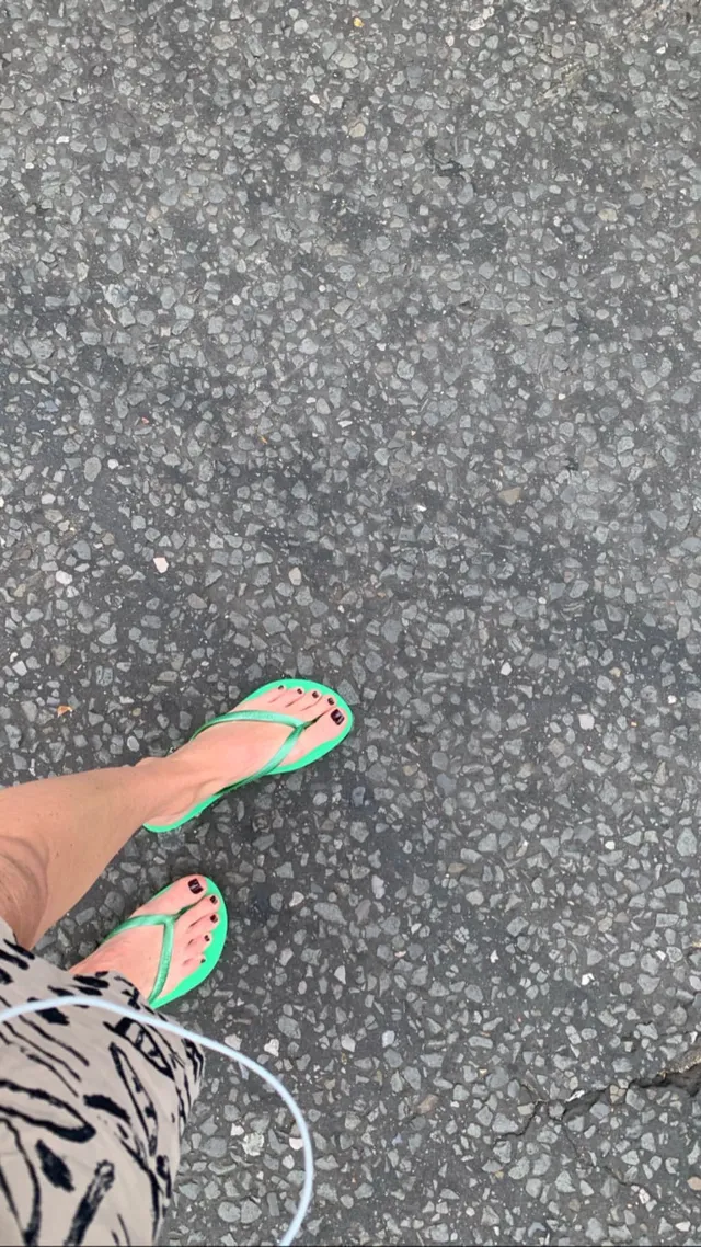 Alice Eve wearing green flat thong sandals on a pavement.