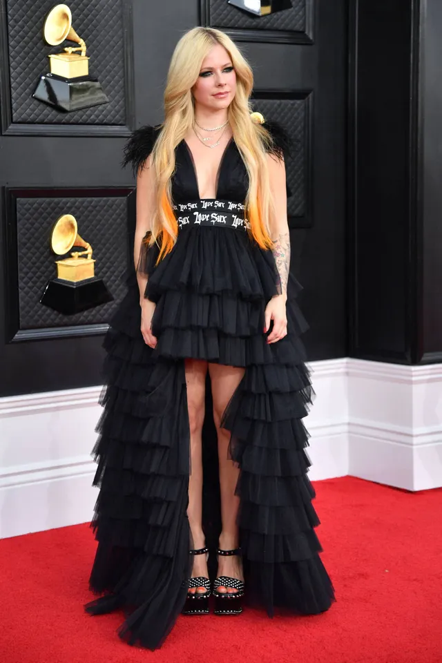 Avril Lavigne standing on a red carpet in a black gown and platform heels.