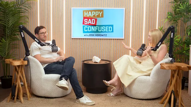 Dakota Fanning speaking with a host during an interview while wearing a pale dress.