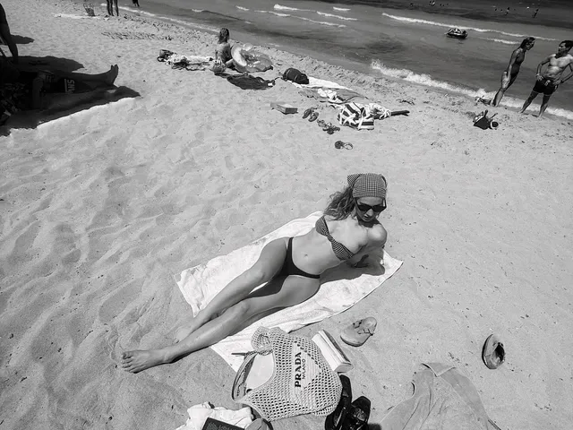 Lily James reclining barefoot on beach sand in a black and white photograph.