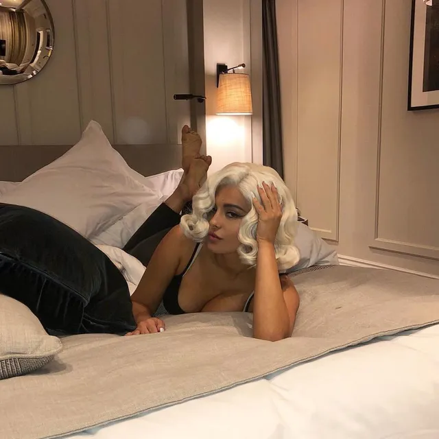 Bebe Rexha reclining on a bed wearing black trousers.