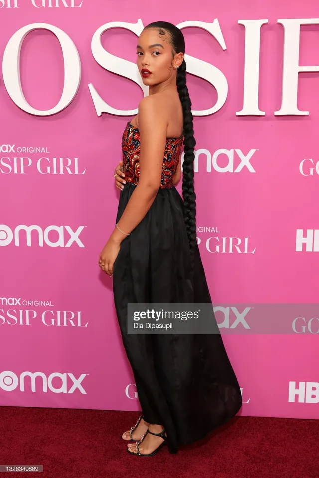 Whitney Peak posing sideways in an embellished top, dark skirt and gold heels.