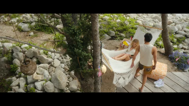 Emily Alyn Lind sitting barefoot in a hammock with a companion nearby.