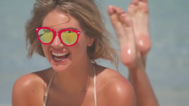 Kate Upton raising one bare foot while wearing bright sunglasses.