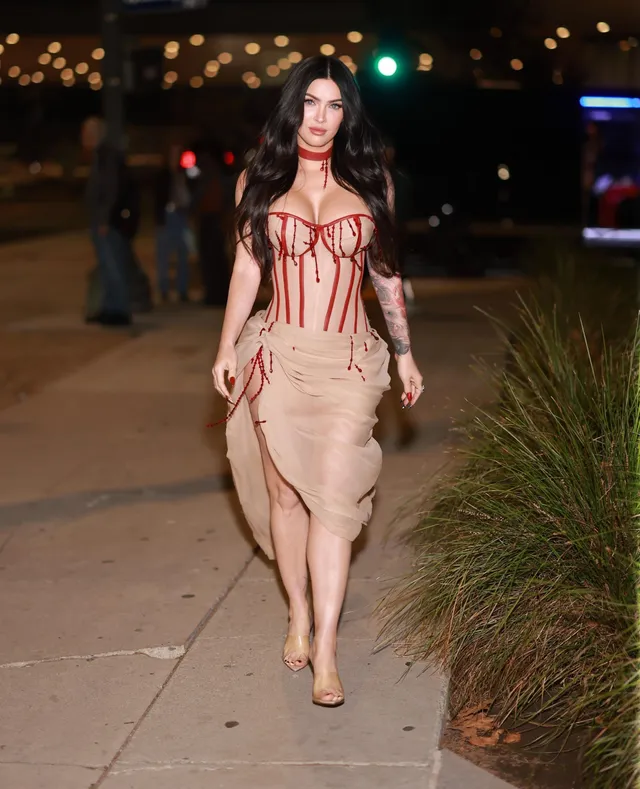 Megan Fox walking outside at night in a pale dress.