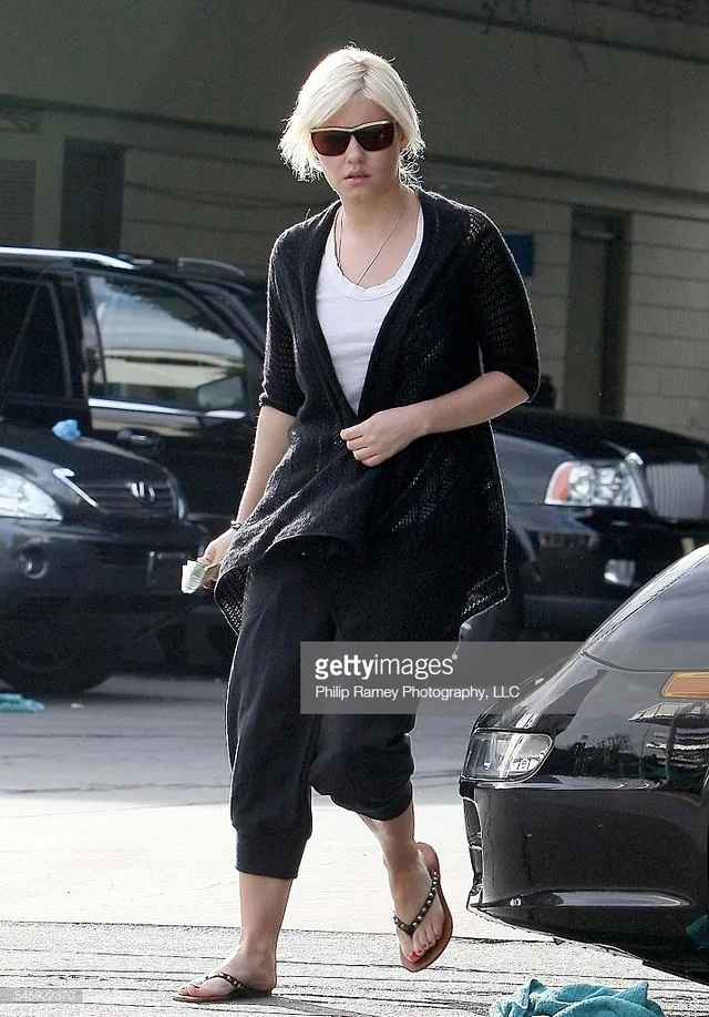 Elisha Cuthbert walking beside a car in cropped trousers and flip-flops.