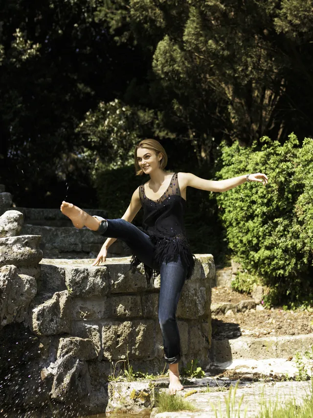 Keira Knightley posing outdoors on stone steps in a black outfit.