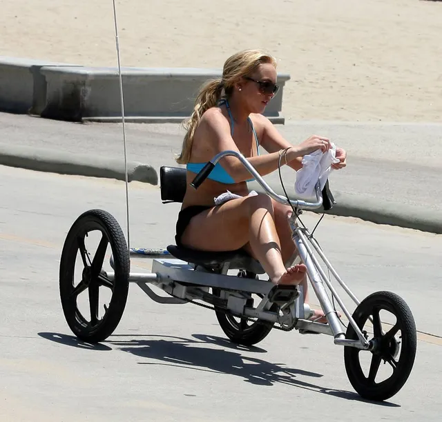 Lindsay Lohan sitting barefoot on a three-wheeled cycle outdoors.