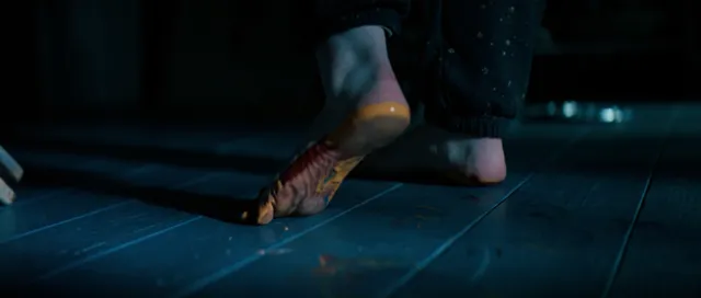 Sophie Thatcher stepping barefoot on a blue-lit tiled floor in a film scene.