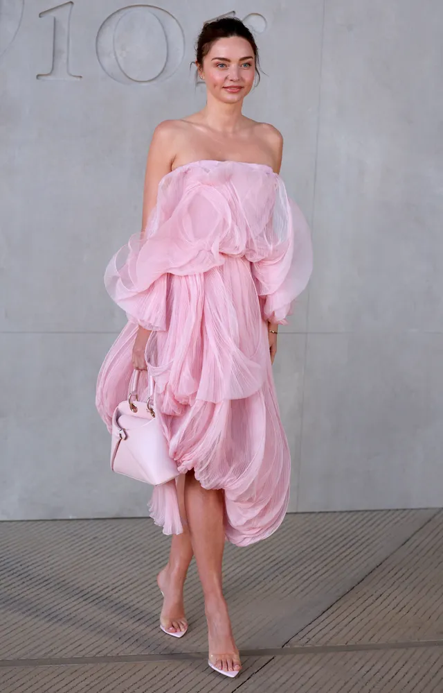 Miranda Kerr a pink dress and pale heels beside a wall.