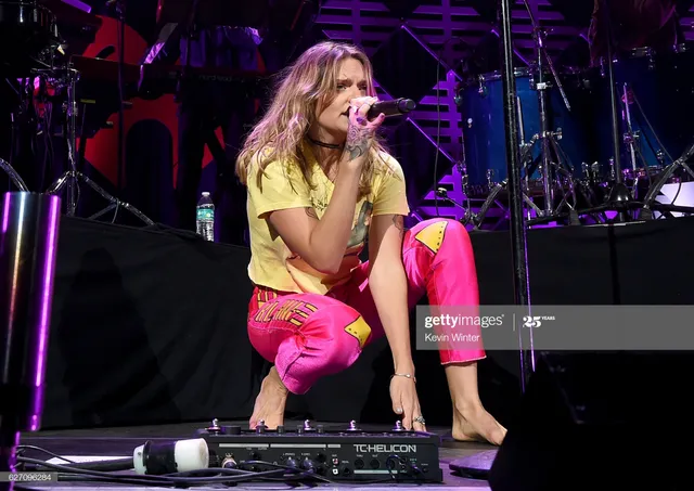 Tove Lo crouching barefoot on stage in pink trousers.