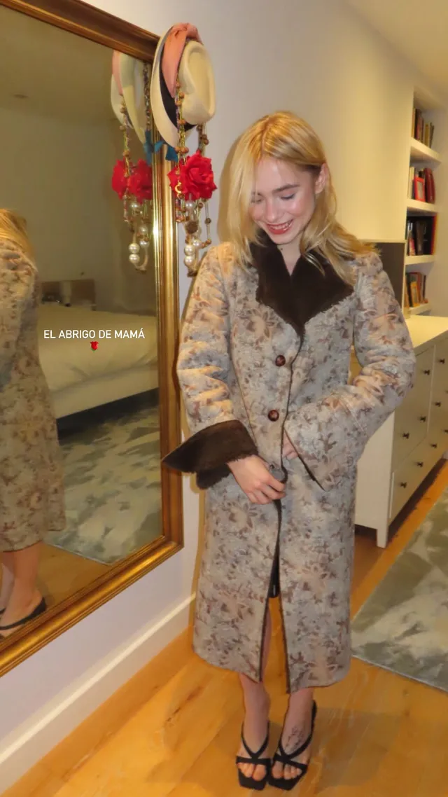 Clara Galle posing indoors in a patterned coat and black heels.